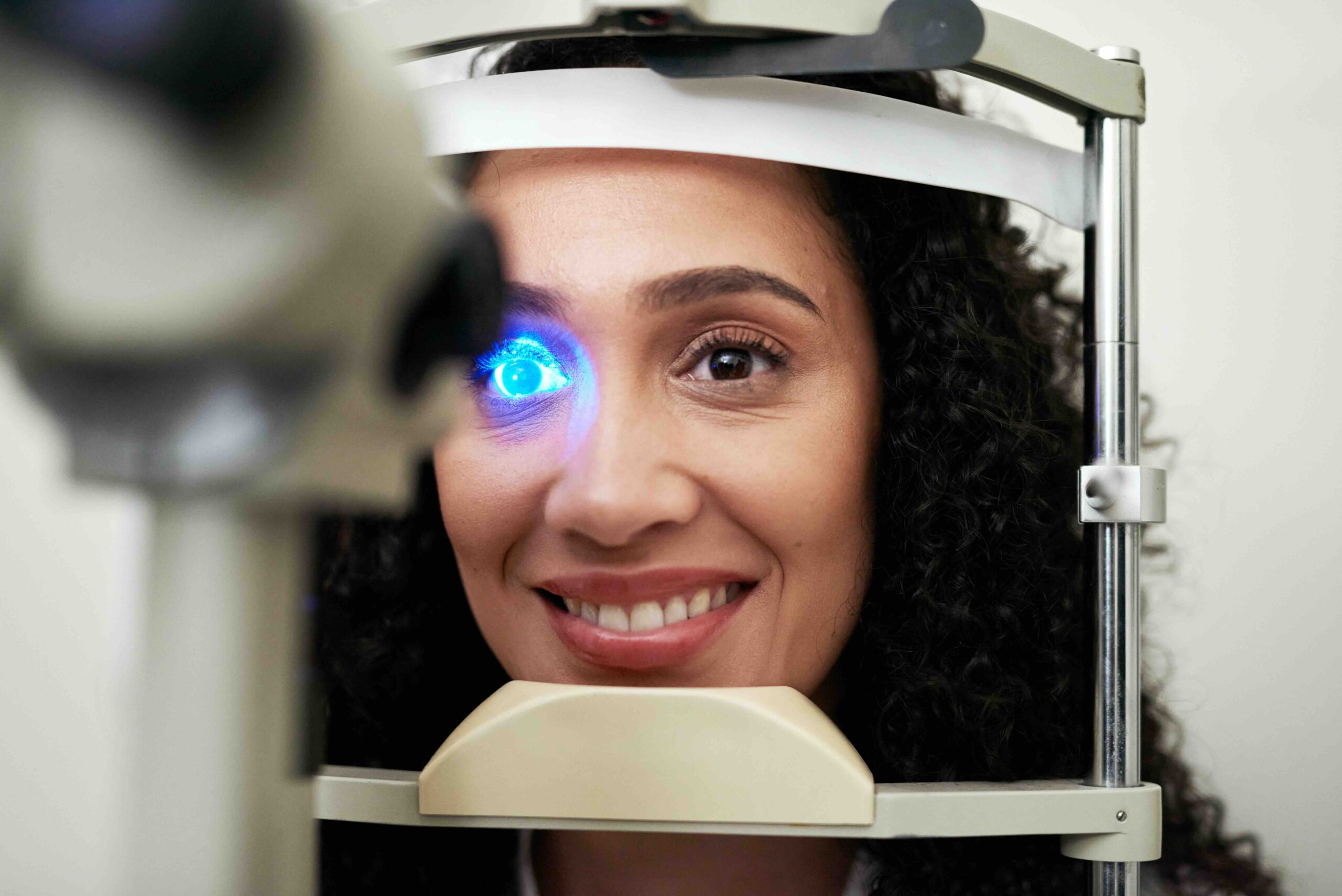 Eye vision and test machine light for scan, optometrist and professional consulting check up. Wellness, patient and consultation for eye exam of black woman at slit lamp with focused smile.